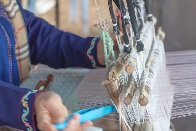 Midsection of a woman weaving textile in a loom